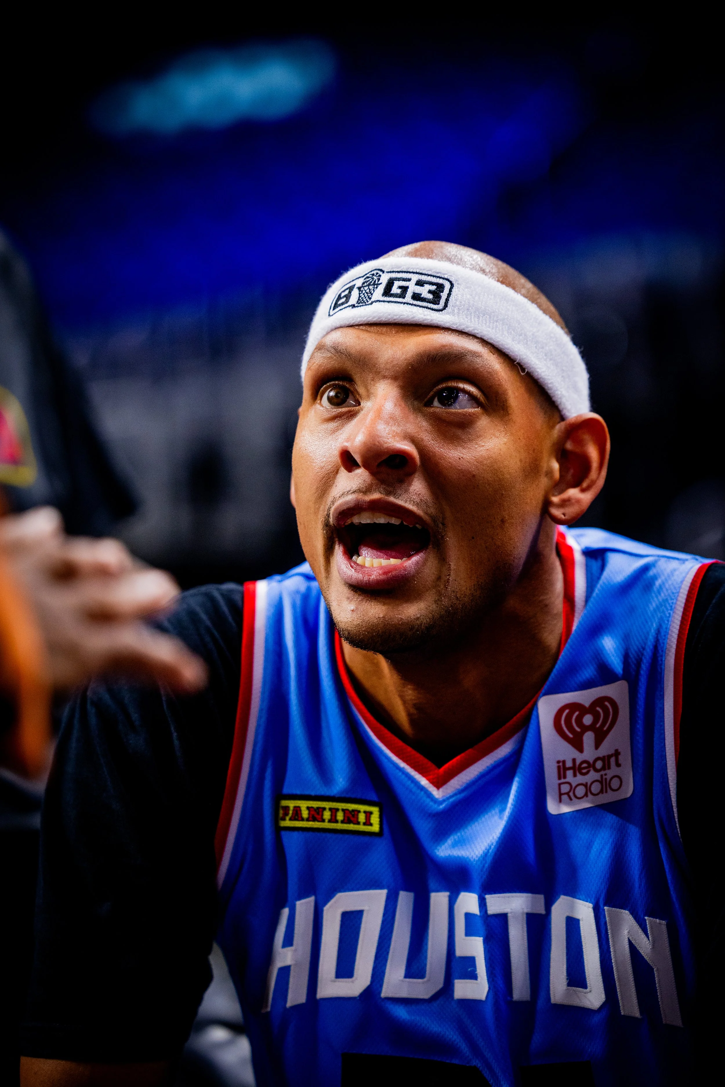 Close-up of a man wearing a Houston Righands basketball jersey and a white headband, appearing excited and taking a selfie in a brightly lit environment.