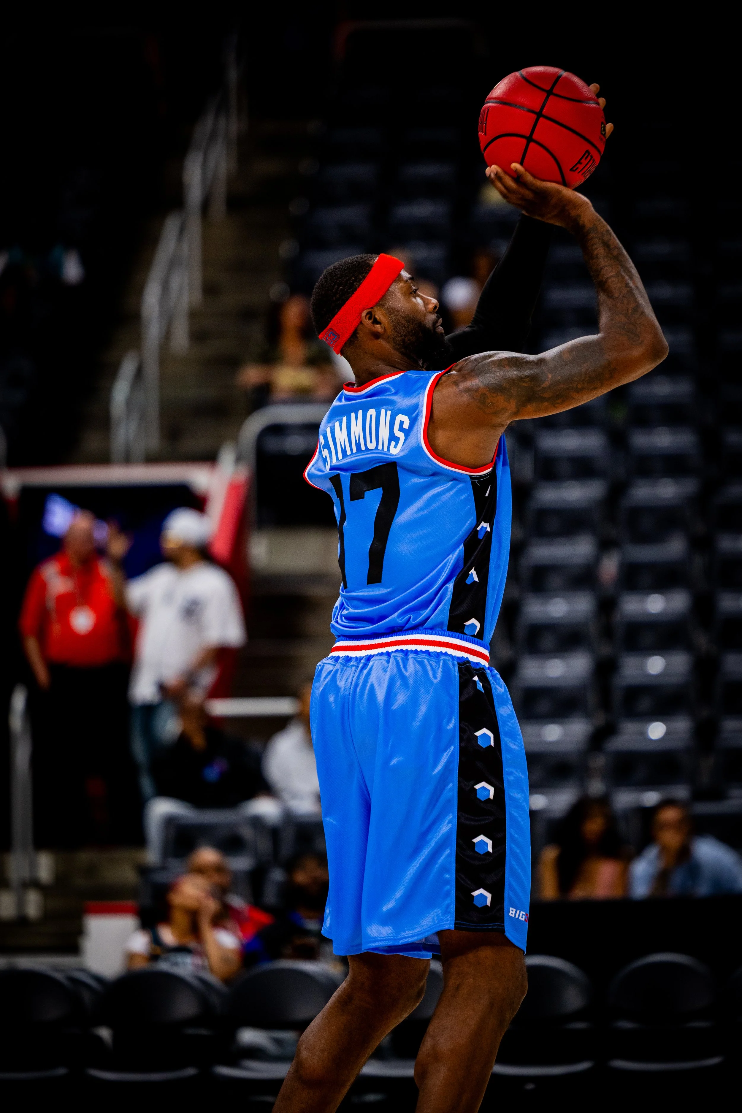 A male basketball player in a blue and black uniform with the name 'Simmons' on the back, preparing to shoot a basketball during a game.