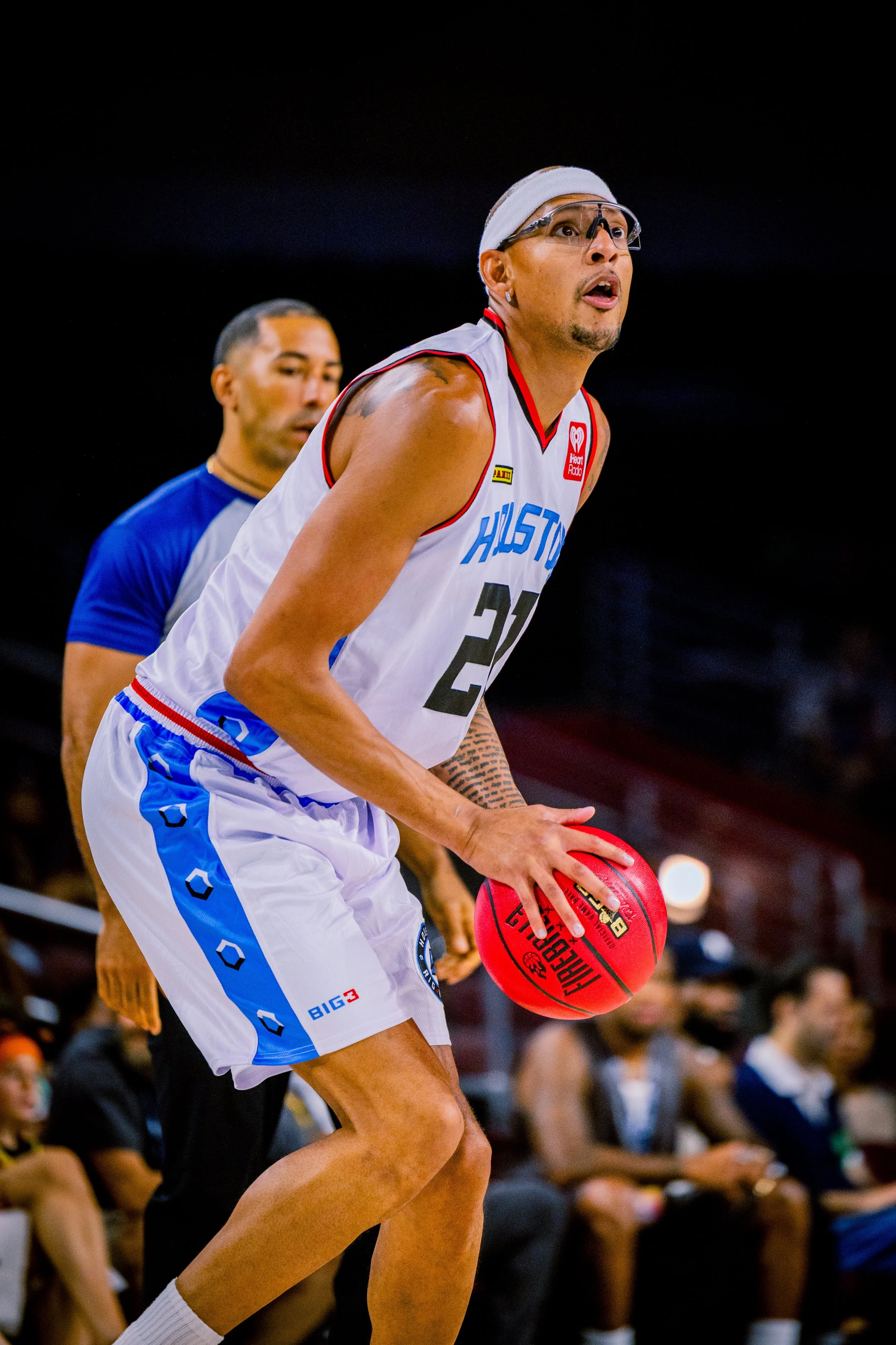 A female basketball player in a white and blue jersey with the number 20, holding a red basketball during a game, with spectators in the background.
