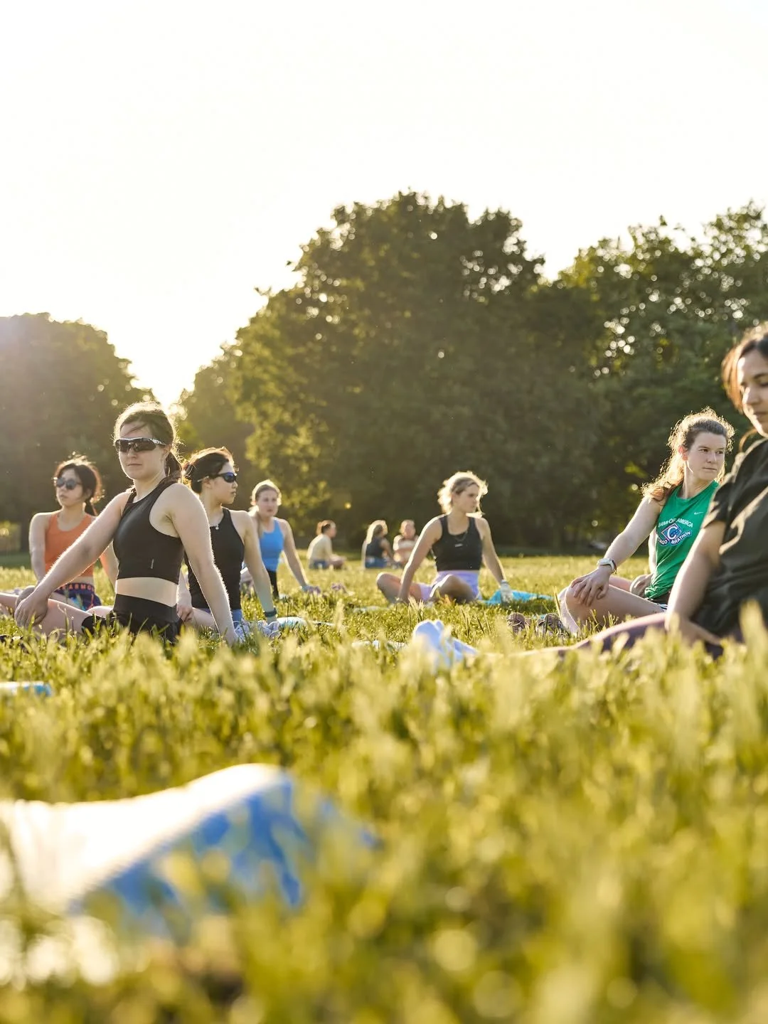 A group of women do yoga in the park, wearing sunglasses