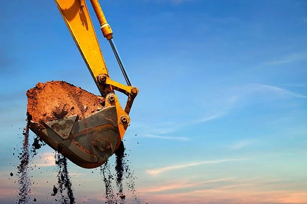 Close-up of a yellow excavator bucket scooping dirt against a blue sky with light clouds.