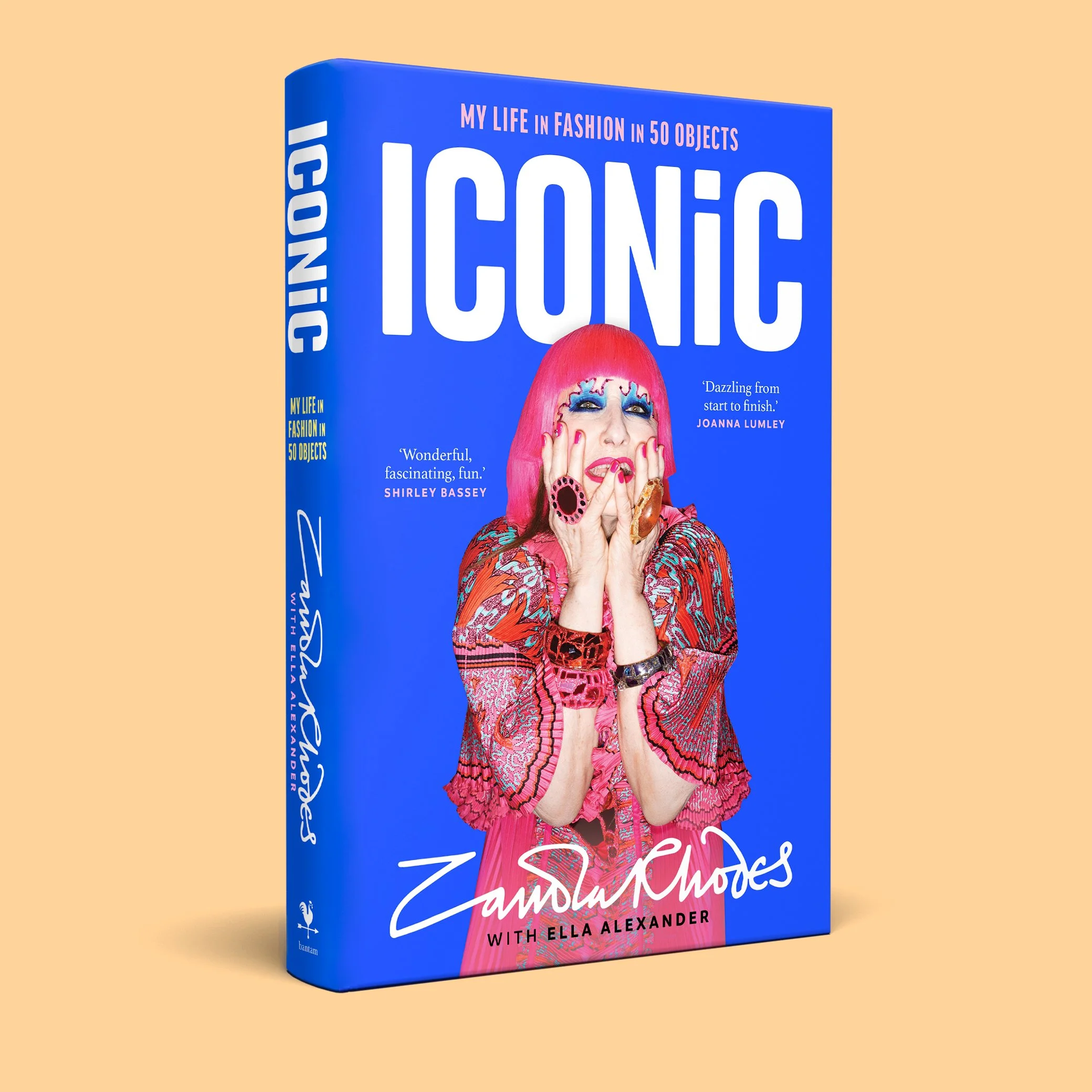 Book 'ICONIC' blue book cover featuring famous textile designer 'Zandra Rhodes' with bright pink hair, colorful makeup, and a patterned outfit, with bold white text and quotes from Shirley Bassey and Joanna Lumley.