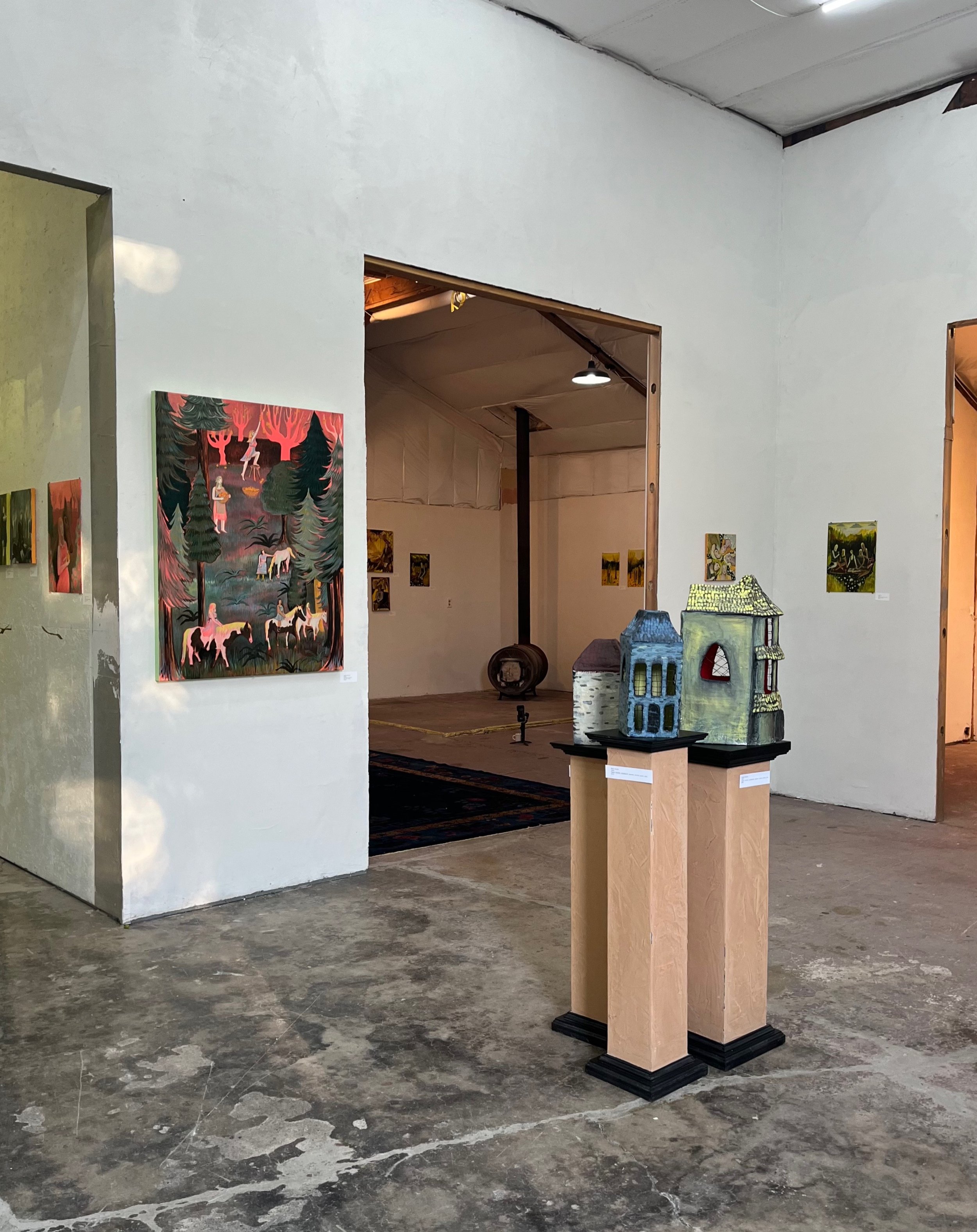 Girl World Exhibition by artist Courtney Costa with paintings on the walls and paper mache sculptures on display, showing a rustic industrial setting with concrete floors and high ceilings.