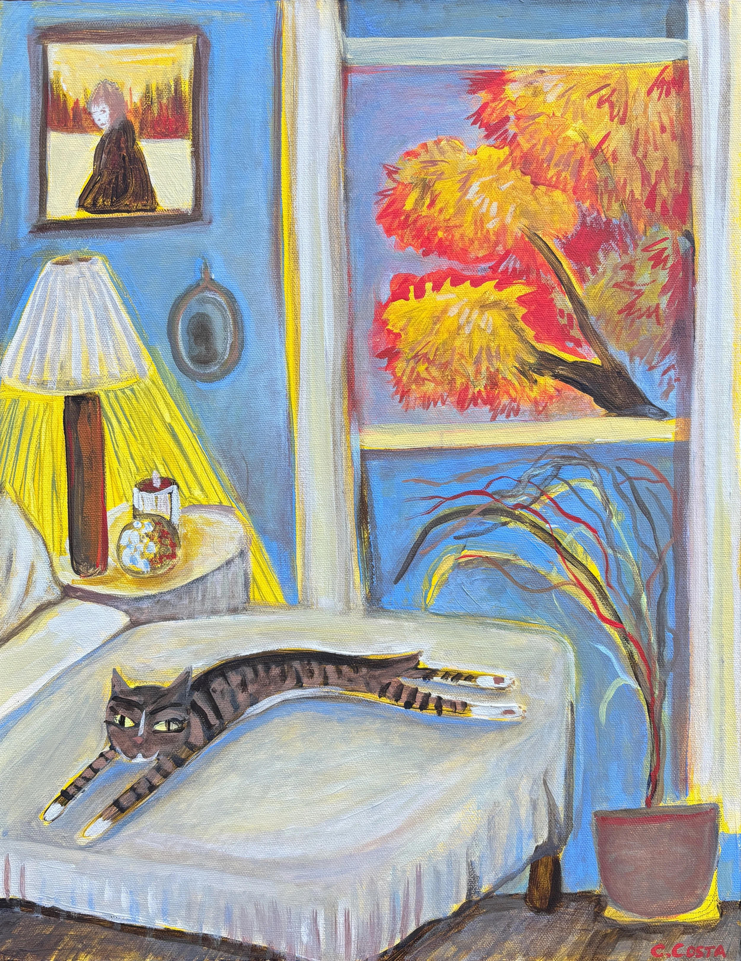 A painting of a cozy interior scene showing a black and brown striped cat lying on a white table with a red mug, a small yellow pumpkin, and a lantern, with a yellow lamp and framed artwork on a nearby wall featuring a woman with long hair and a colorful outdoor landscape view through the window.