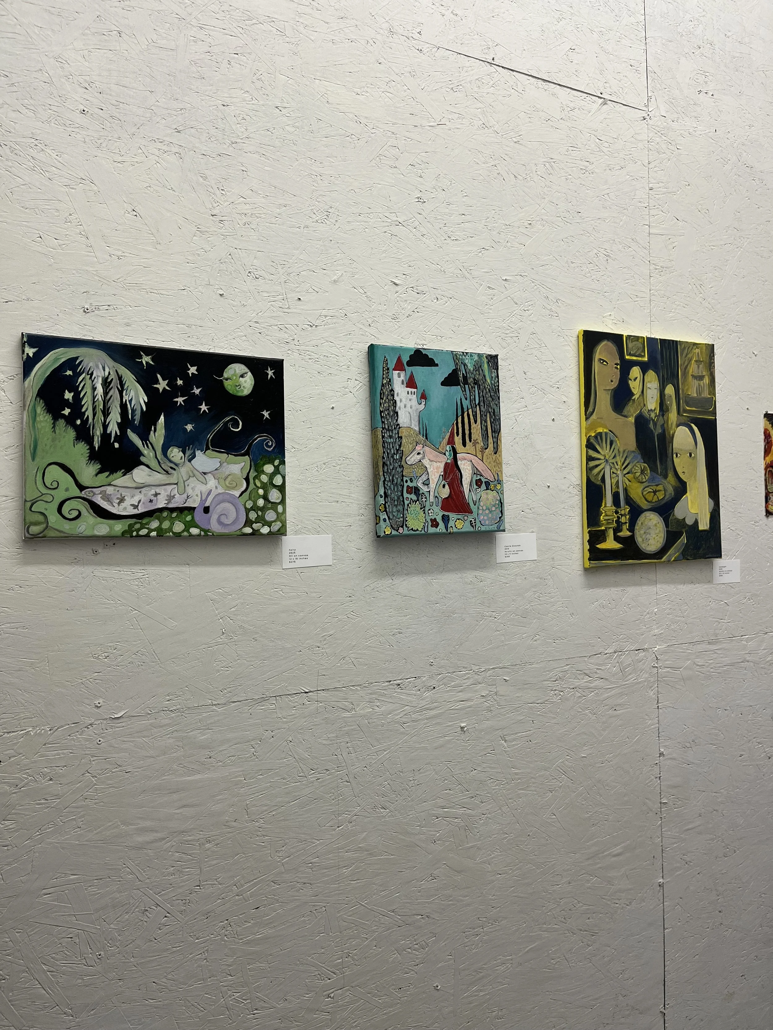 Three colorful paintings hanging on a textured white wall in an art gallery.