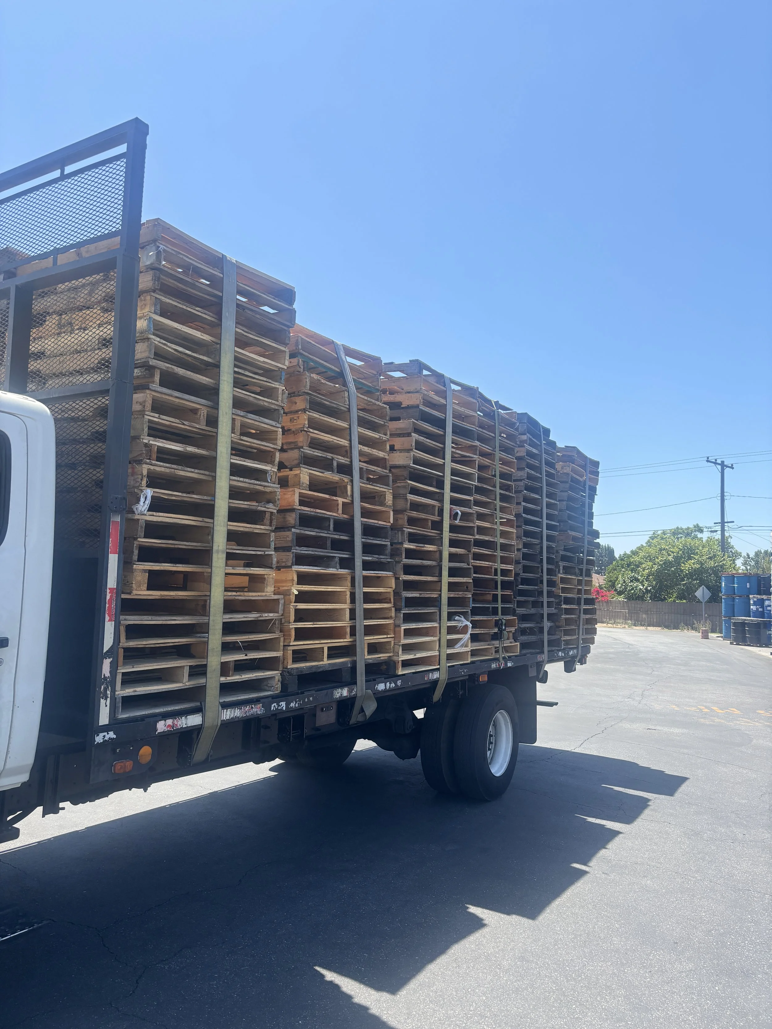 A flatbed truck carrying stacked wooden pallets parked outdoors under a bright blue sky.