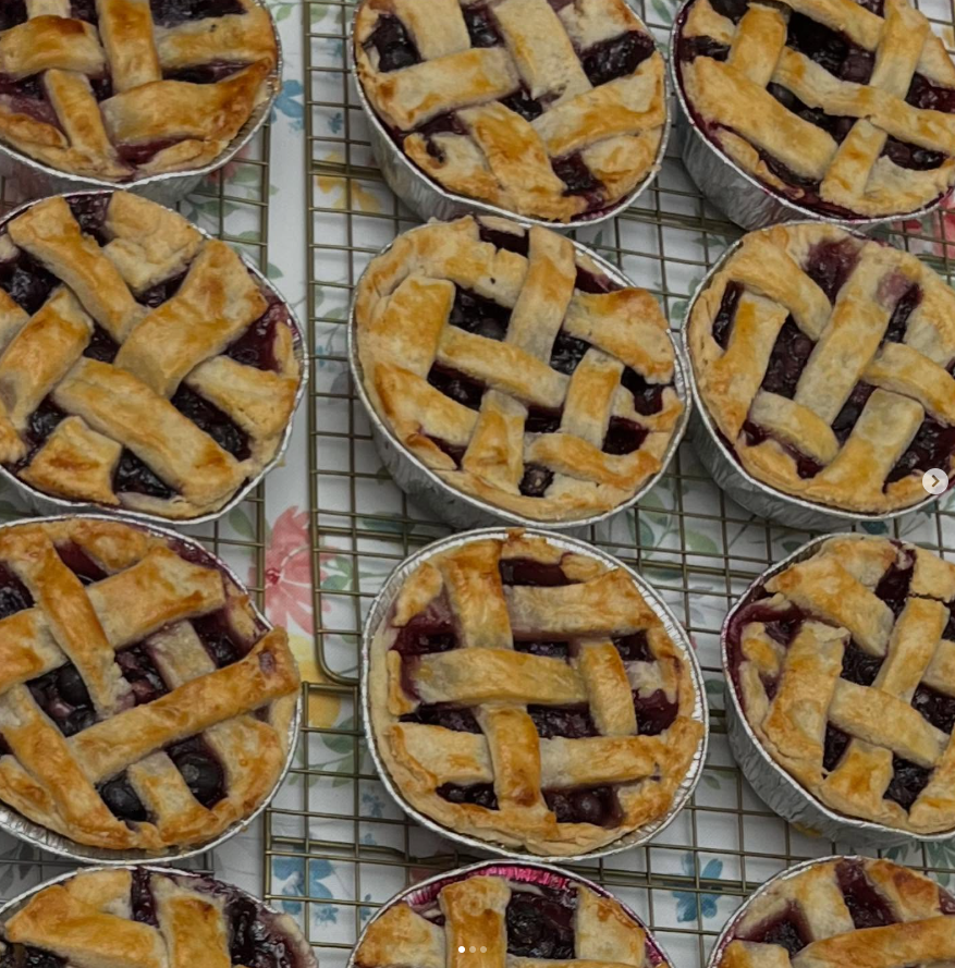Several small berry pies with lattice crusts cooling on a wire rack.