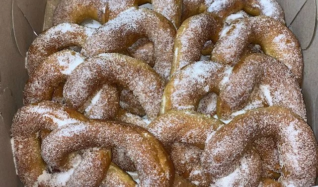 A basket of dusted powdered sugar donuts arranged in a box.