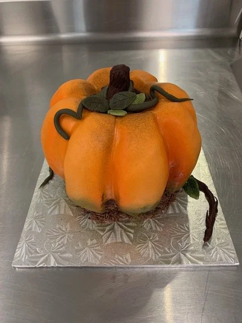 Cake designed to look like a pumpkin with green leaves, a brown stem, and vines.