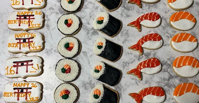 Assorted decorated cookies on a marble surface, including some with birthday messages, sushi, and Japanese torii gate designs.