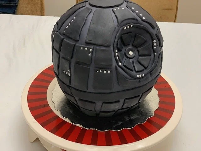 Cake designed to look like the Death Star from Star Wars, placed on a white table with a red and black striped base.