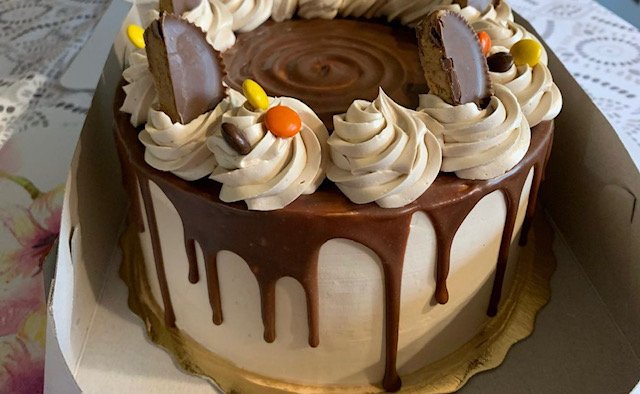 A decorated chocolate and vanilla birthday cake with chocolate glaze dripping down the sides, topped with swirl frosting, colorful candies, and chocolate pieces.