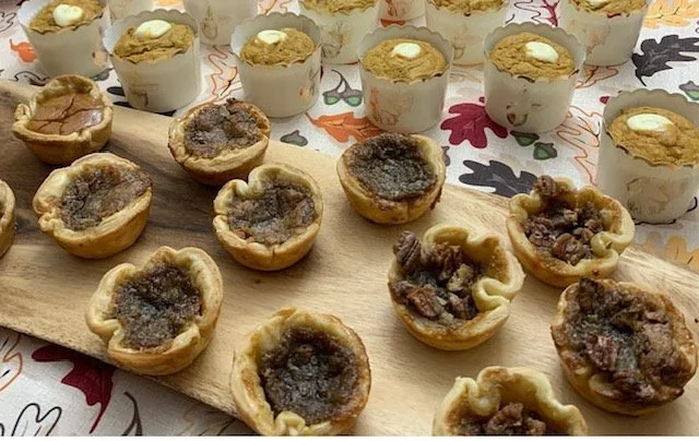 Miniature savory pies with meat filling on a wooden board, surrounded by cupcakes with white frosting.