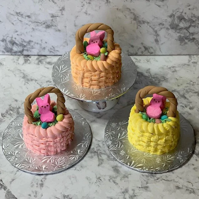 Three colorful Easter basket-shaped cakes, each with a pink Peppa Pig figure and decorated with pastel-colored candies, on silver trays against a marble background.