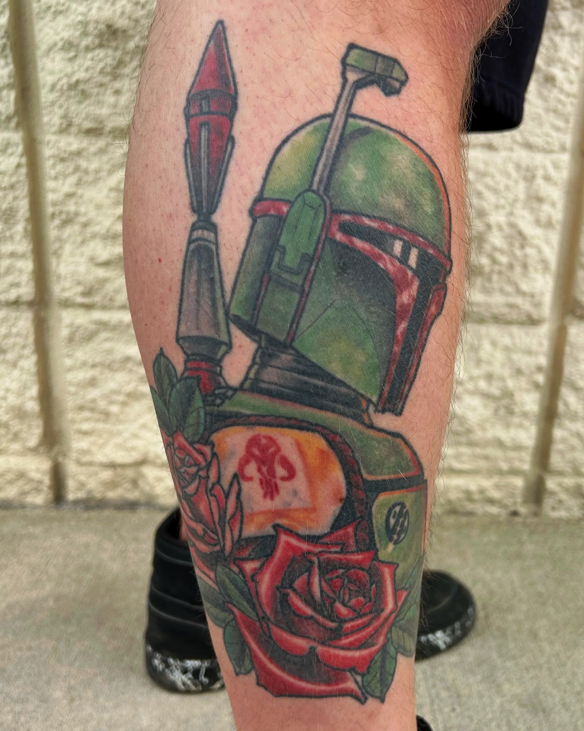 A tattoo on a person's arm depicting a sci-fi style helmet with a green and red color scheme, and two missiles or rocket-like objects with red tips and grey bodies.