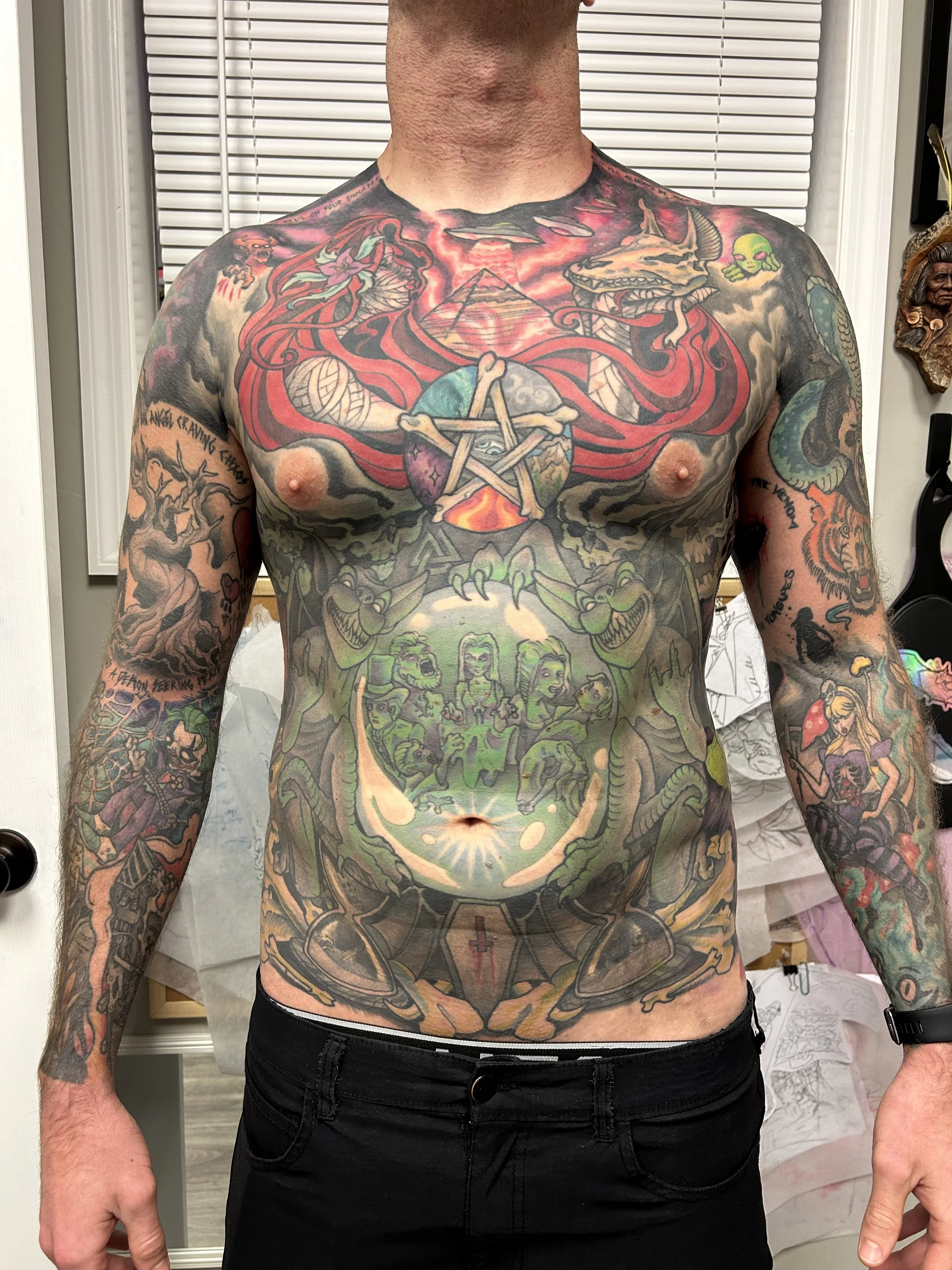 Colorful full-chest tattoo featuring a dragon, a skull with horns, snakes, a pentagram, and various mythical and fantastical elements, including a scene with human-like figures at the bottom.