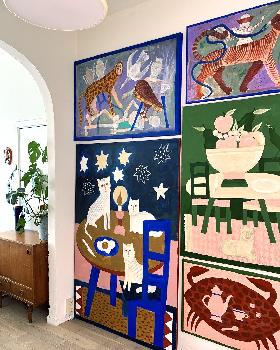 Colorful wall art featuring animals, stars, and kitchen scenes, including cats, a tiger, a leopard, and a bowl of apples, in a vibrant, folk-art style.