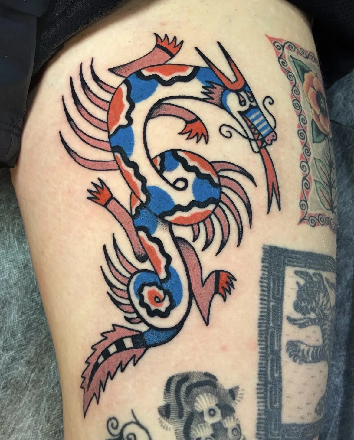 Tattoo of a colorful lizard with blue, orange, and white patterns, surrounded by abstract lines and designs.