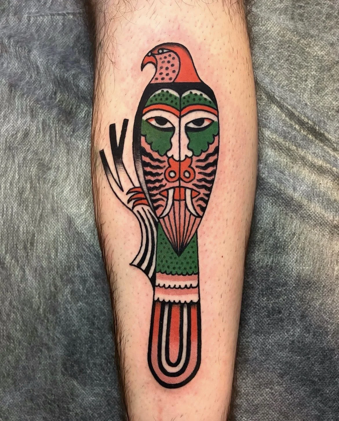 Tattoo of a stylized bird with a human face, colorful feathers, and geometric patterns on a person's arm.
