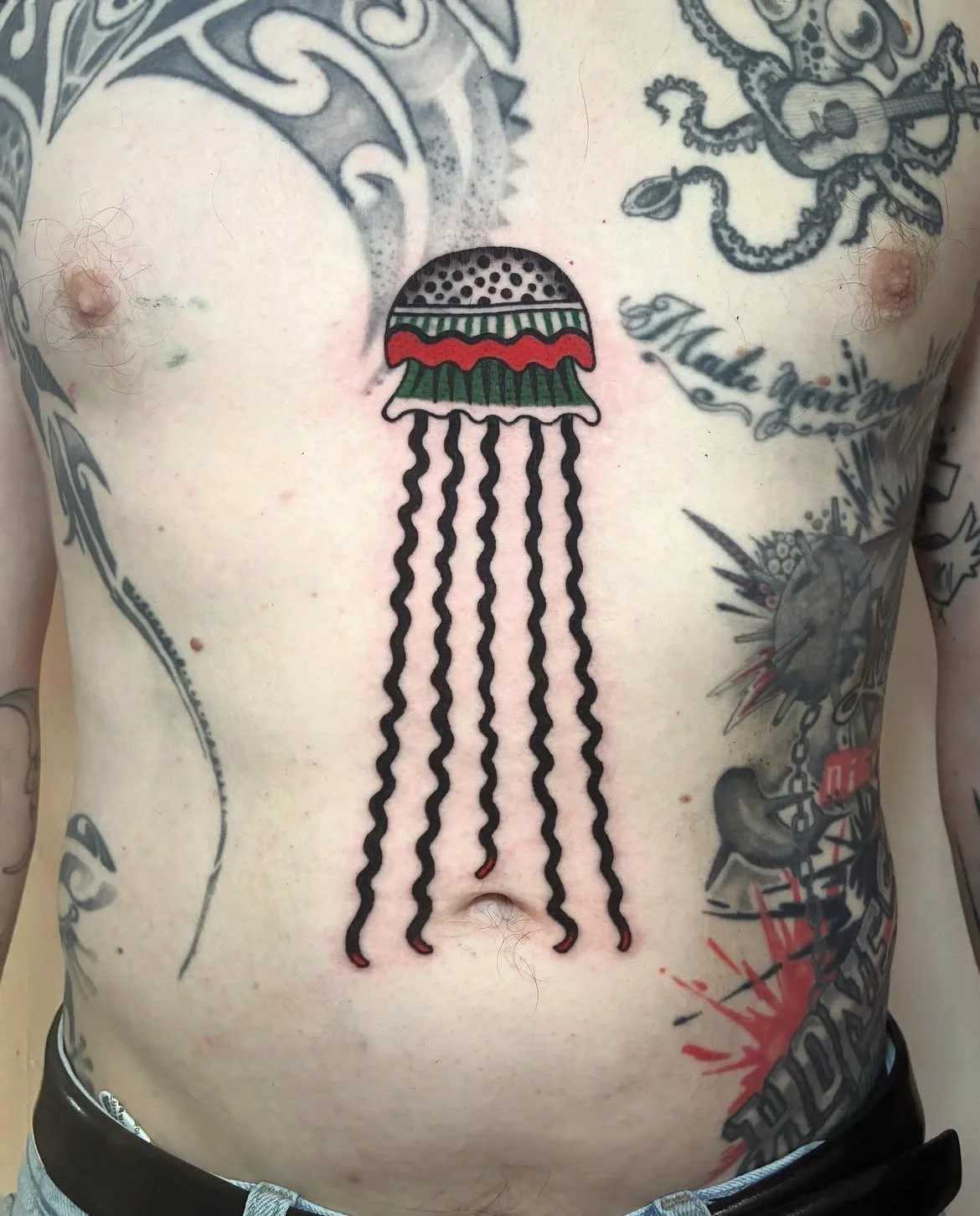 Tattoo of a stylized jellyfish with a patterned bell and wavy tentacles on a person's chest.