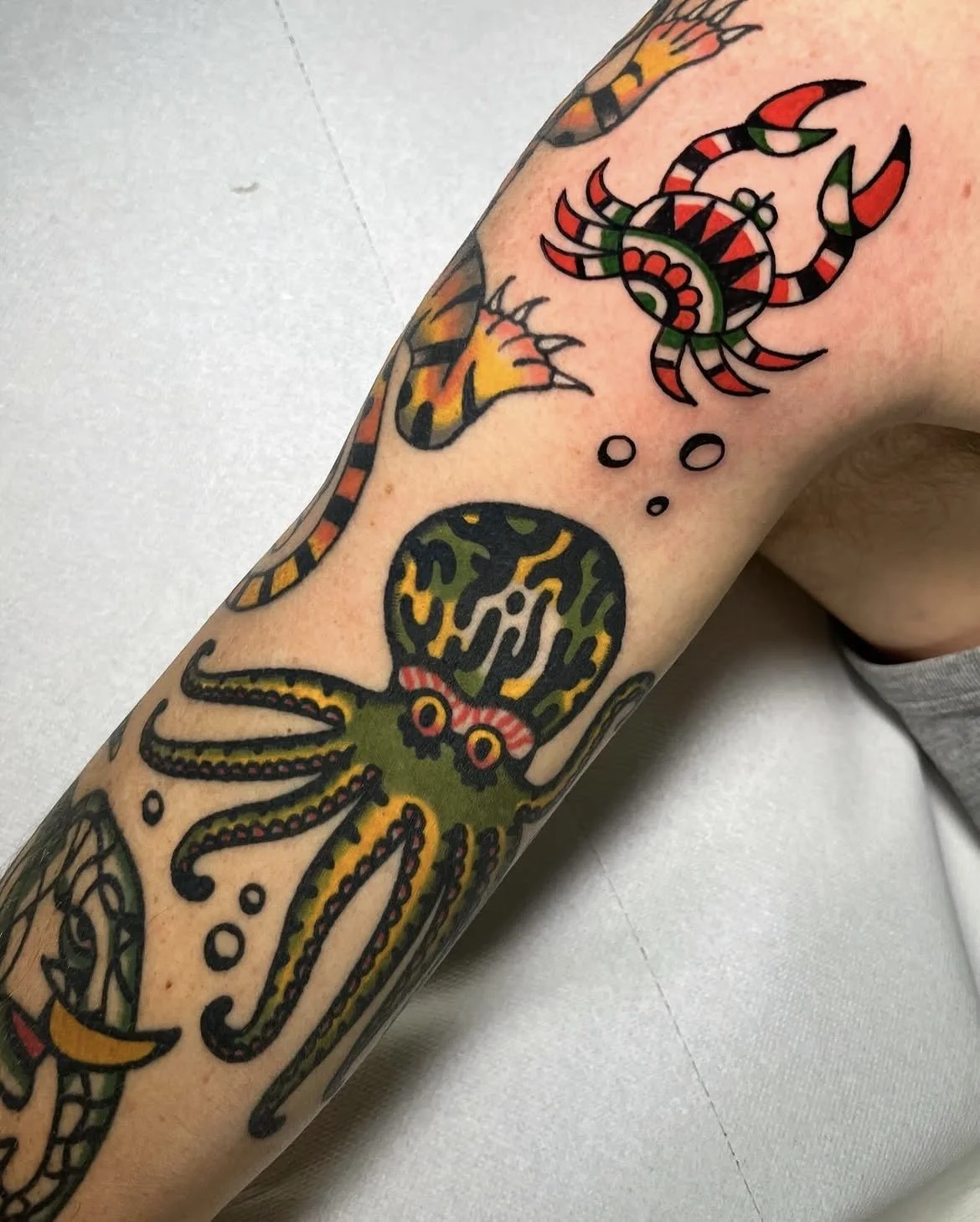 Tattoo of a colorful octopus on a person's arm, with a thought bubble containing a snake and a lizard.