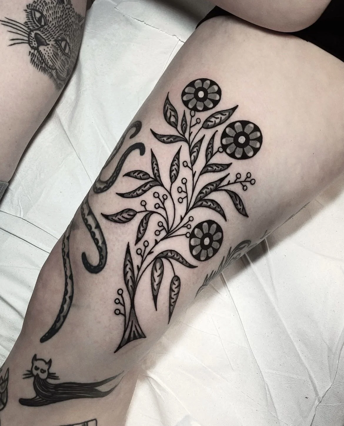 Black ink floral tattoo on person's leg featuring a leafy branch with three stylized flowers.