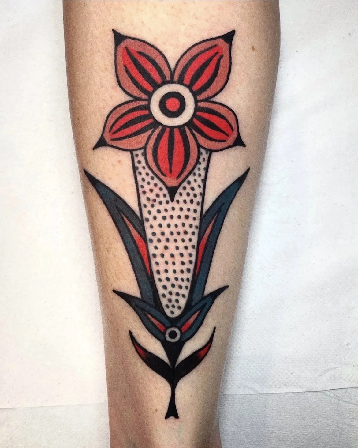 Tattoo of a stylized flower with red petals and black outlines on a person's arm.