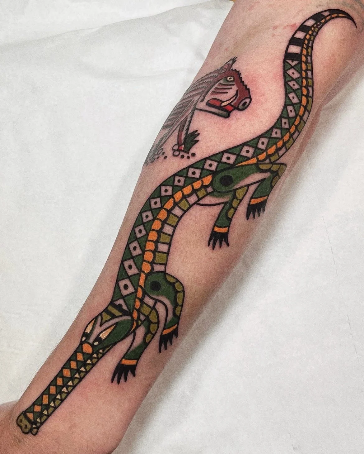 Tattoo of a colorful snake with green, orange, and black diamond patterns, coiled around the arm, with a traditional wolf head tattoo above.