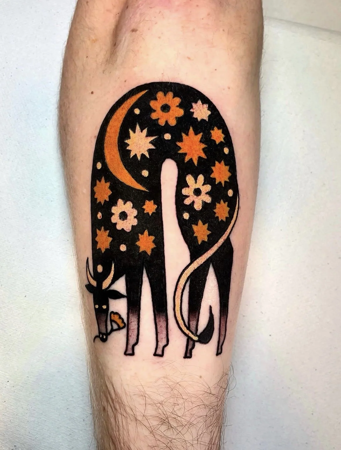 Tattoo of a giraffe with a starry night sky on its body, featuring stars, a crescent moon, and flowers, on a person's arm.