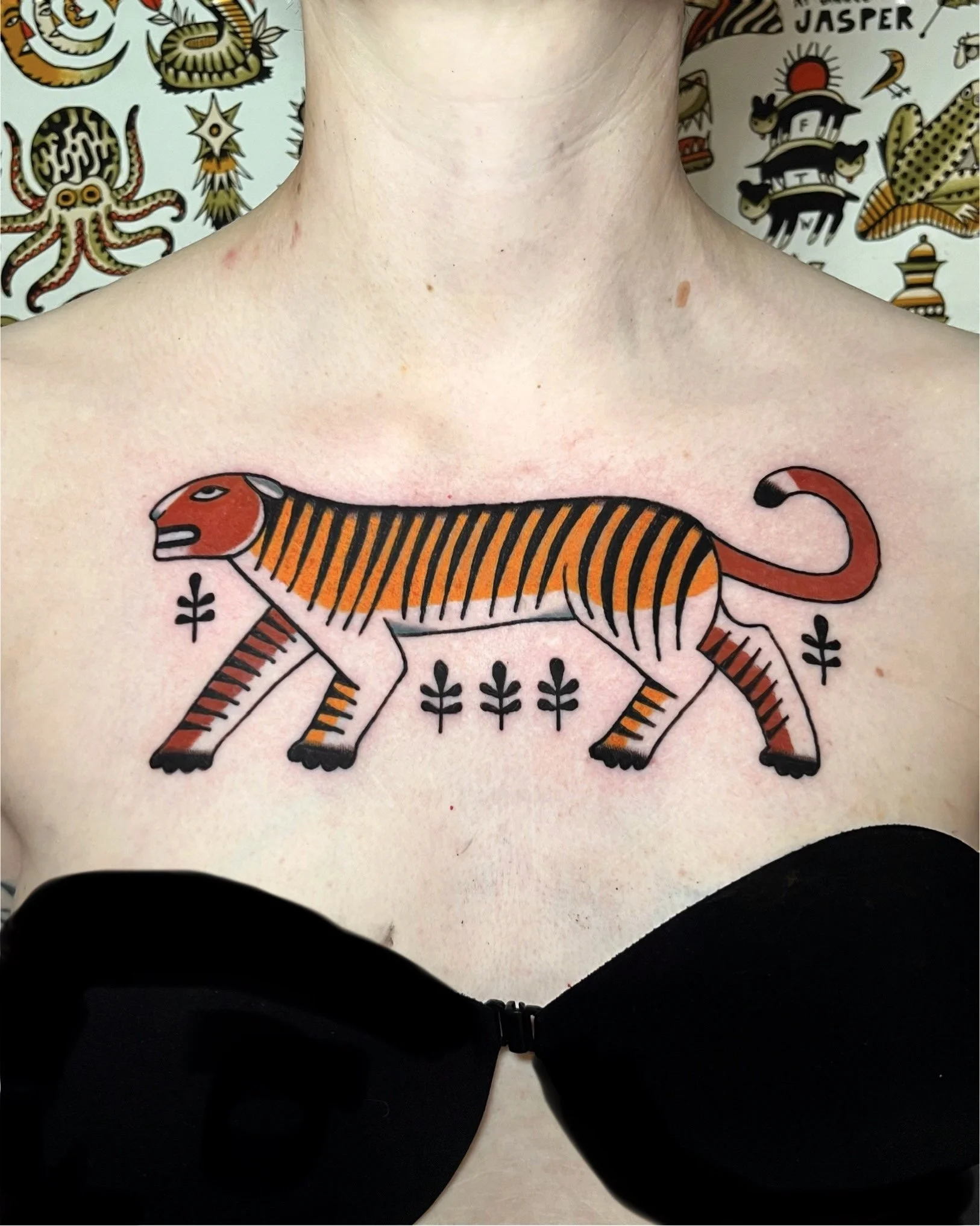 A tattoo of a stylized tiger with orange and black stripes on a person's chest, surrounded by decorative elements.