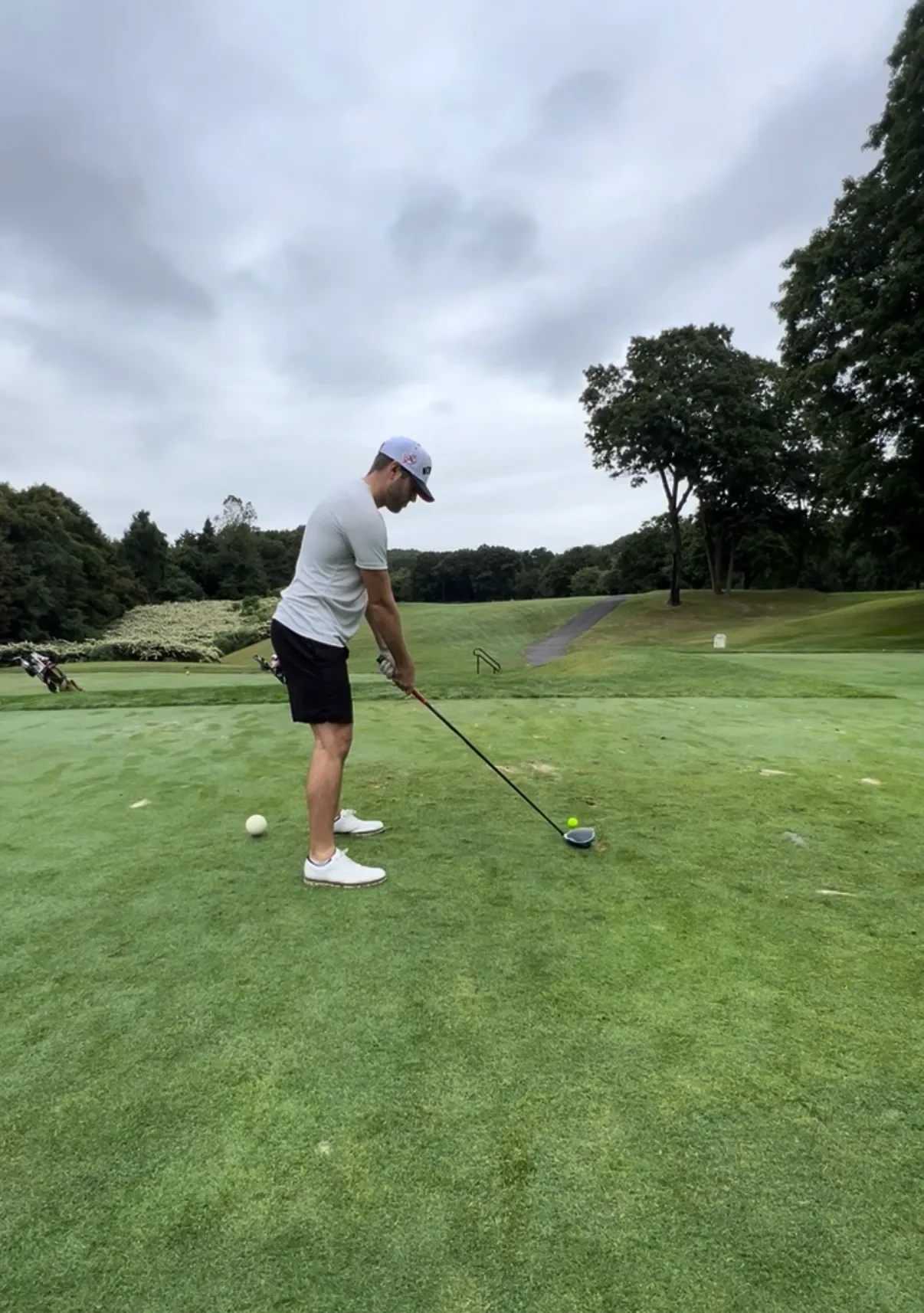 Man playing golf on a golf course, preparing to hit the ball with a golf club under a cloudy sky.