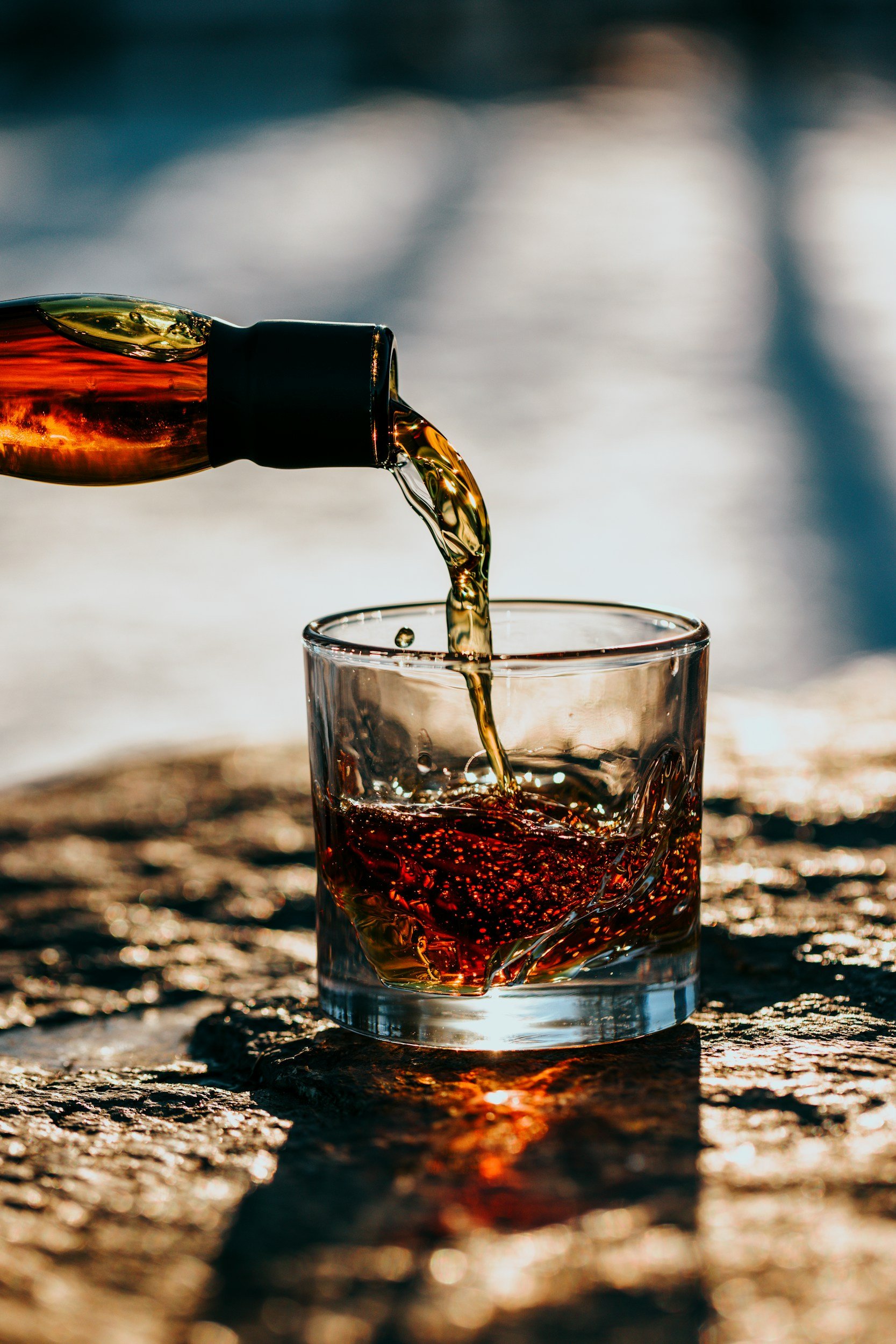 A glass being filled with a dark liquid from a dropper at sunset.