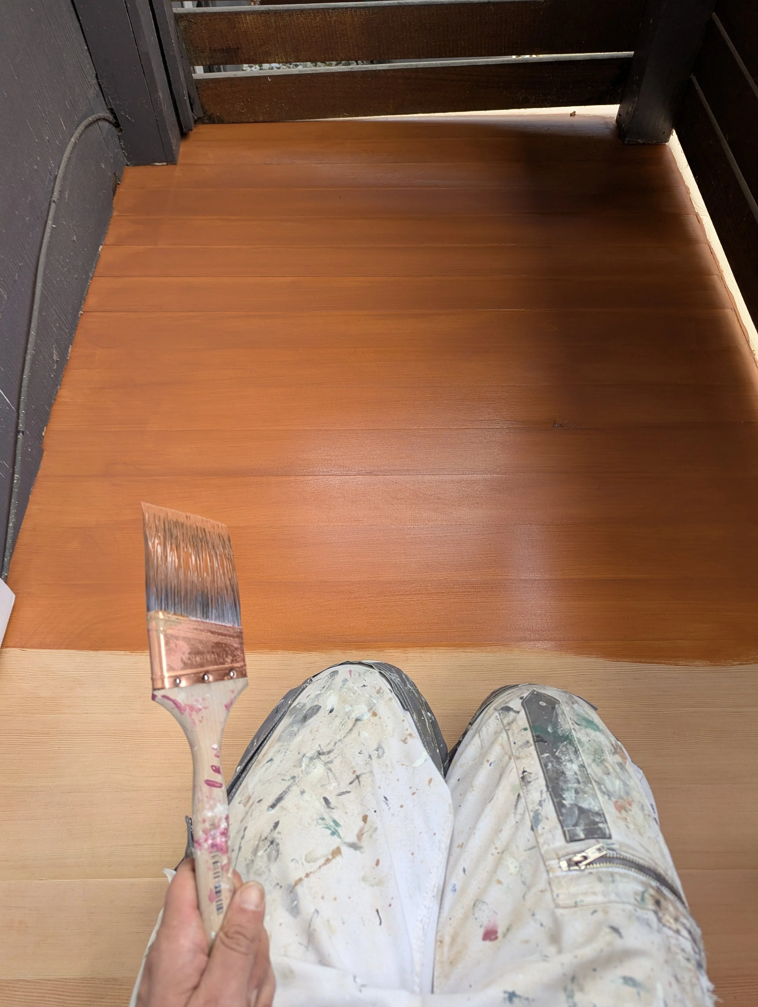 picture of a painter's knees in the process of staining a porch