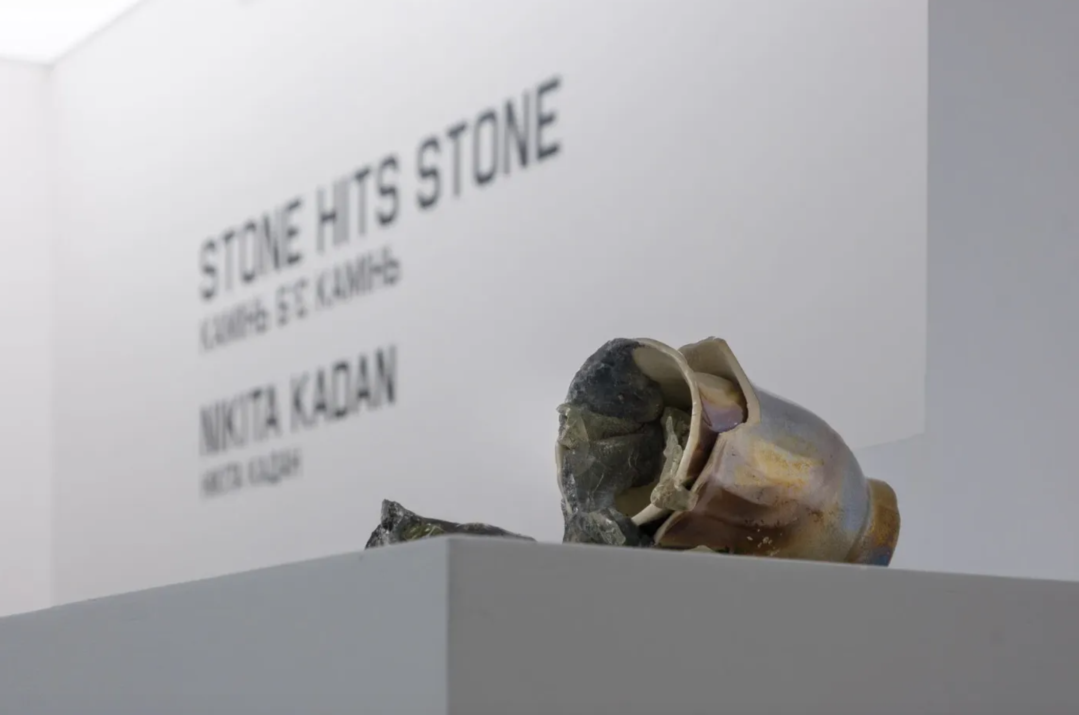 Close-up of a mounted stone skull sculpture in front of a white wall with text reading 'Stone Huts Stone' and other information.