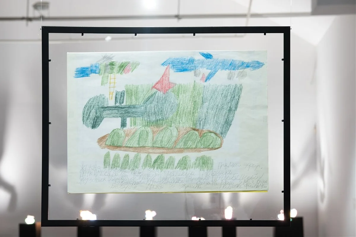 Child's colored drawing of a tank with a helicopter and plane flying above, written in Russian at the bottom.