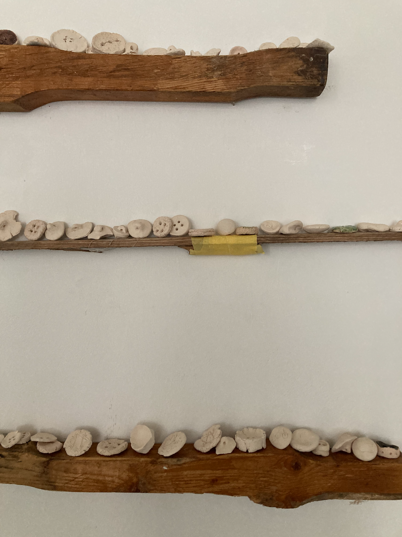 Three horizontal wooden planks mounted on a white wall, each decorated with various small stones and pebbles.