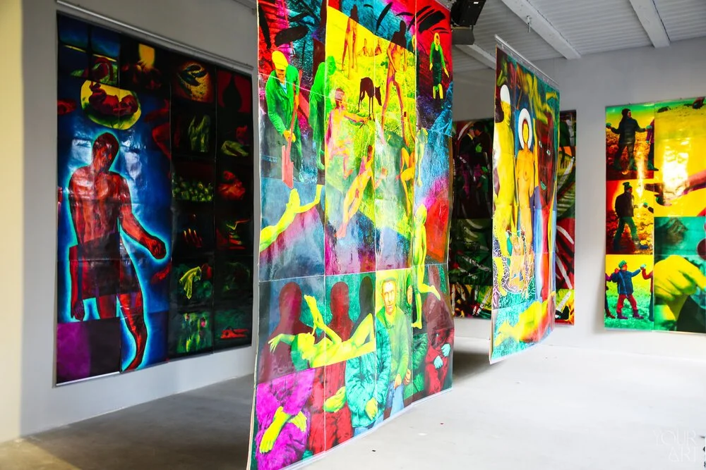 Gallery wall with vibrant, colorful paintings depicting various scenes of people, animals, and abstract patterns.