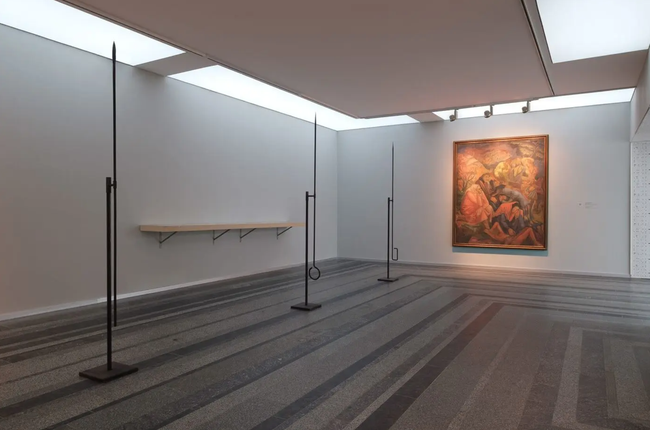 Contemporary art gallery with minimalist design, large skylights, and sculptures resembling gymnastic rings on black stands, along with a framed painting on the wall.