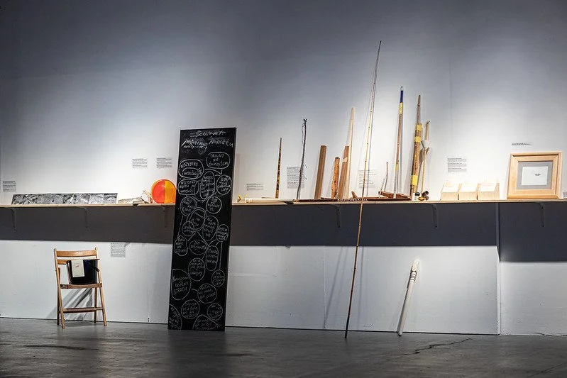 Museum exhibit shelf displaying various objects including model ships, a chalkboard, a framed picture, and a chair.
