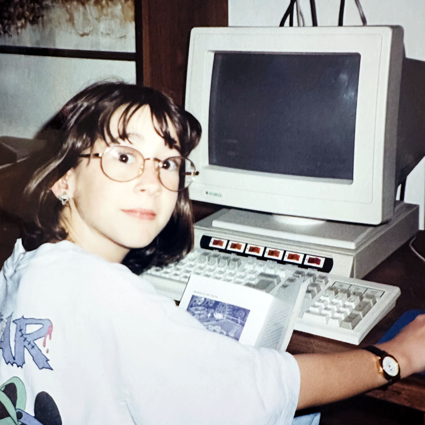 Childhood photo of Finn Thurber wearing glasses, sitting at an old desktop computer and holding a small booklet