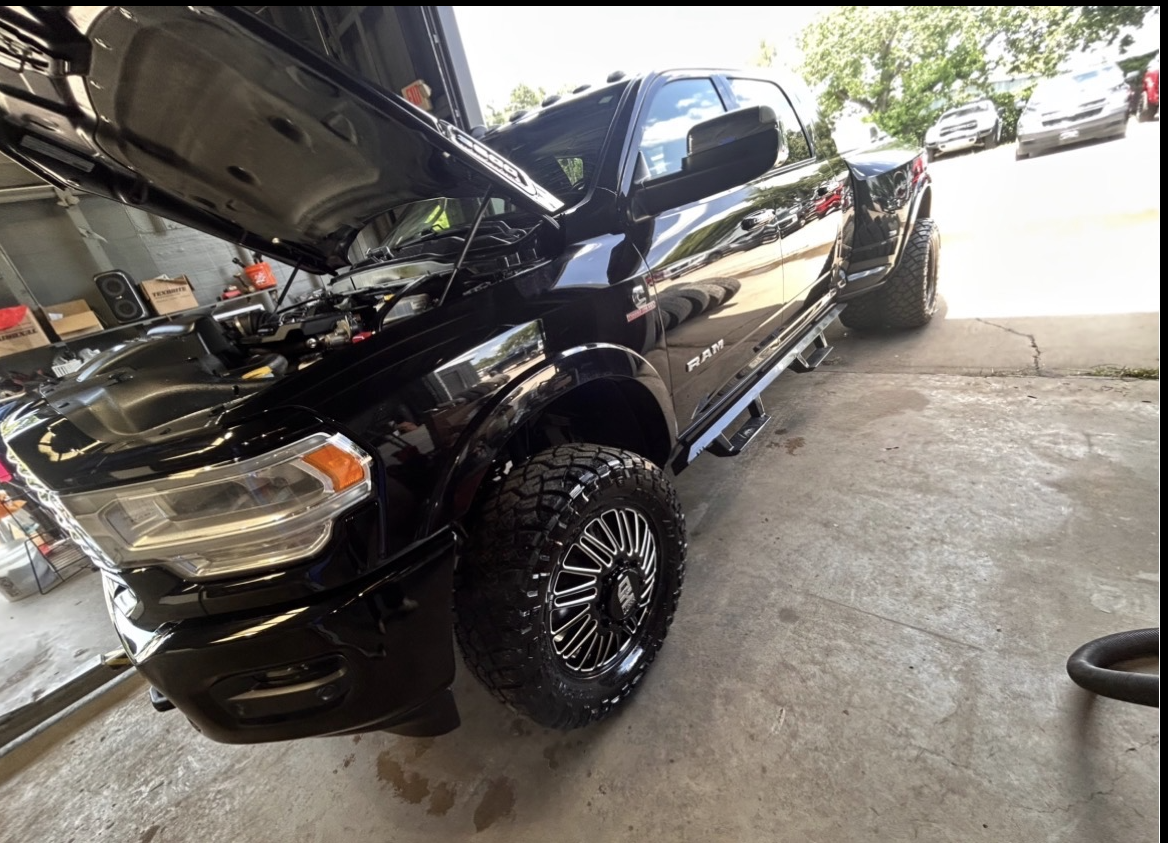 Black pickup truck with lifted suspension and large off-road tires inside a garage, with the hood open.