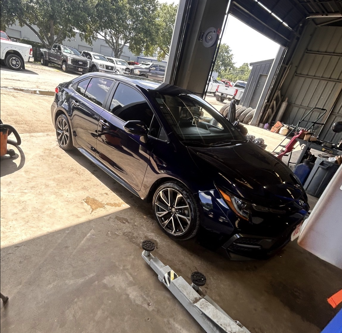 Black sedan parked inside a garage with other parked vehicles outside.