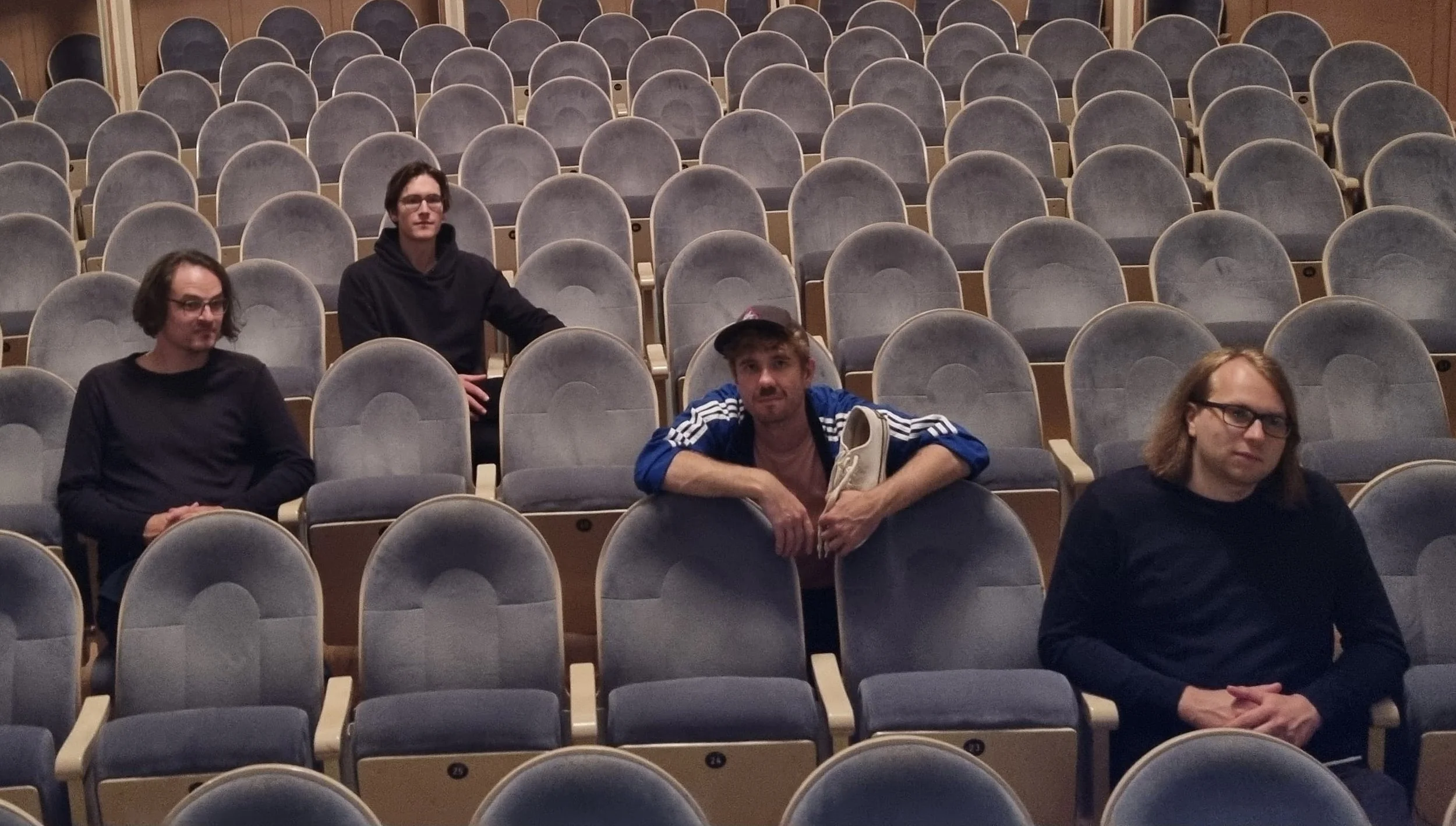 Max Autsch Quartett. Fünf Menschen sitzen in einem leeren Theater mit mehreren Reihen von grauen Sesseln.