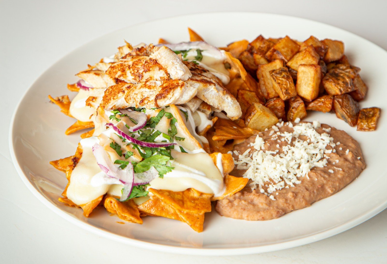 Plato de chilaquiles con salsa chipotle, cebolla, cilantro, papas fritas y frijoles refritos con queso
