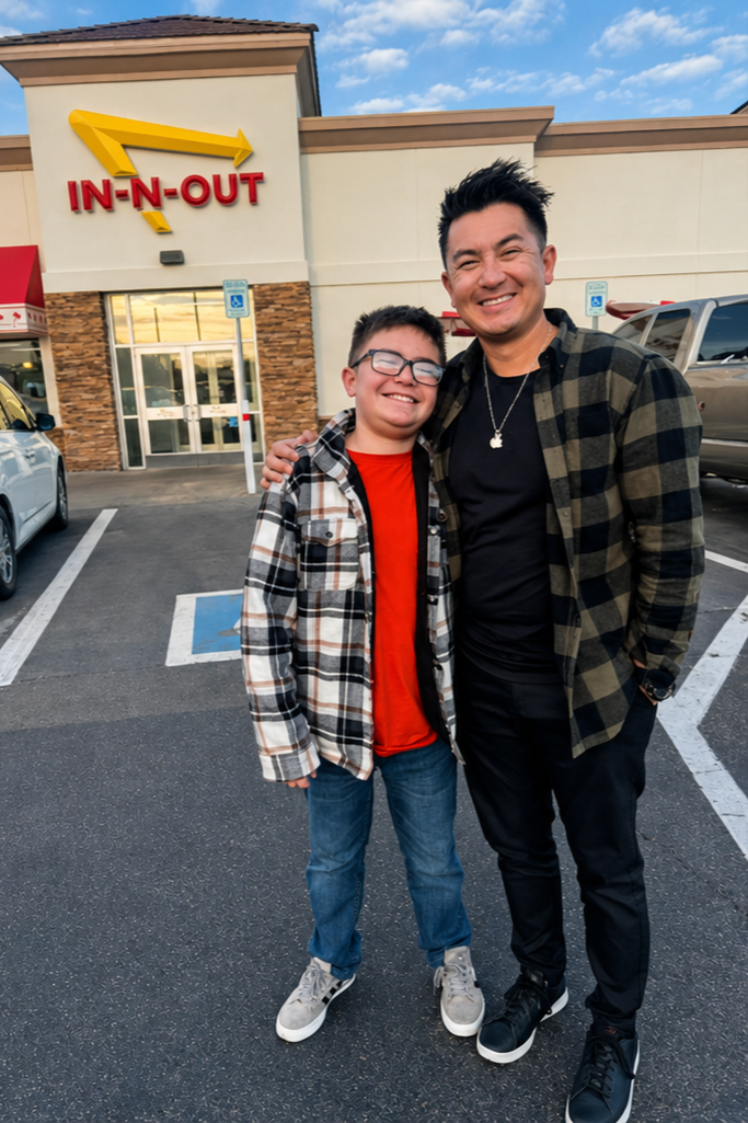 Two people standing in a parking lot in front of an In-N-Out Burger fast-food restaurant, smiling and posing for the photo.