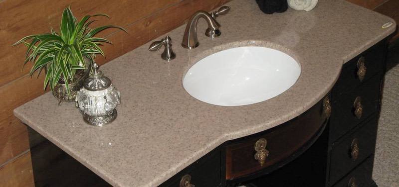Bathroom vanity with a speckled beige countertop, white oval sink, silver fixtures, green plant in a silver pot, and decorative items.