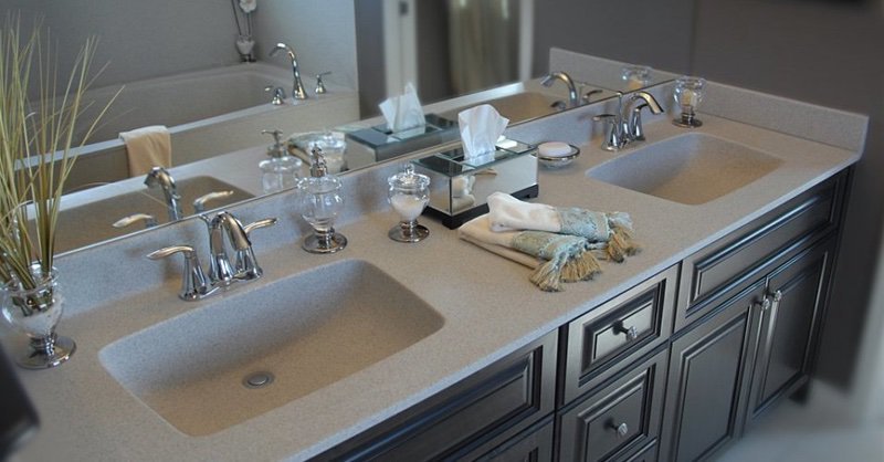 Bathroom double sink vanity with silver fixtures, tissue box, glasses, and decorative towels, reflected in a mirror.