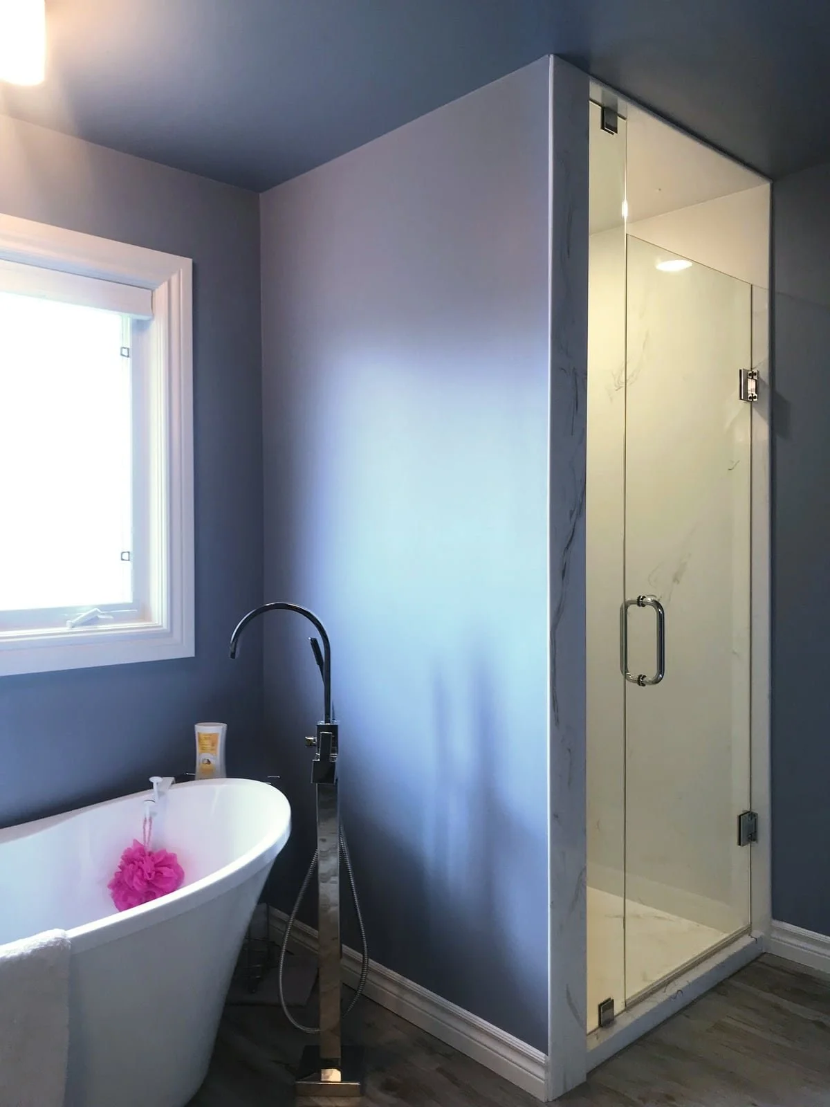 Bathroom with freestanding bathtub, window, gray walls, and a glass shower enclosure.