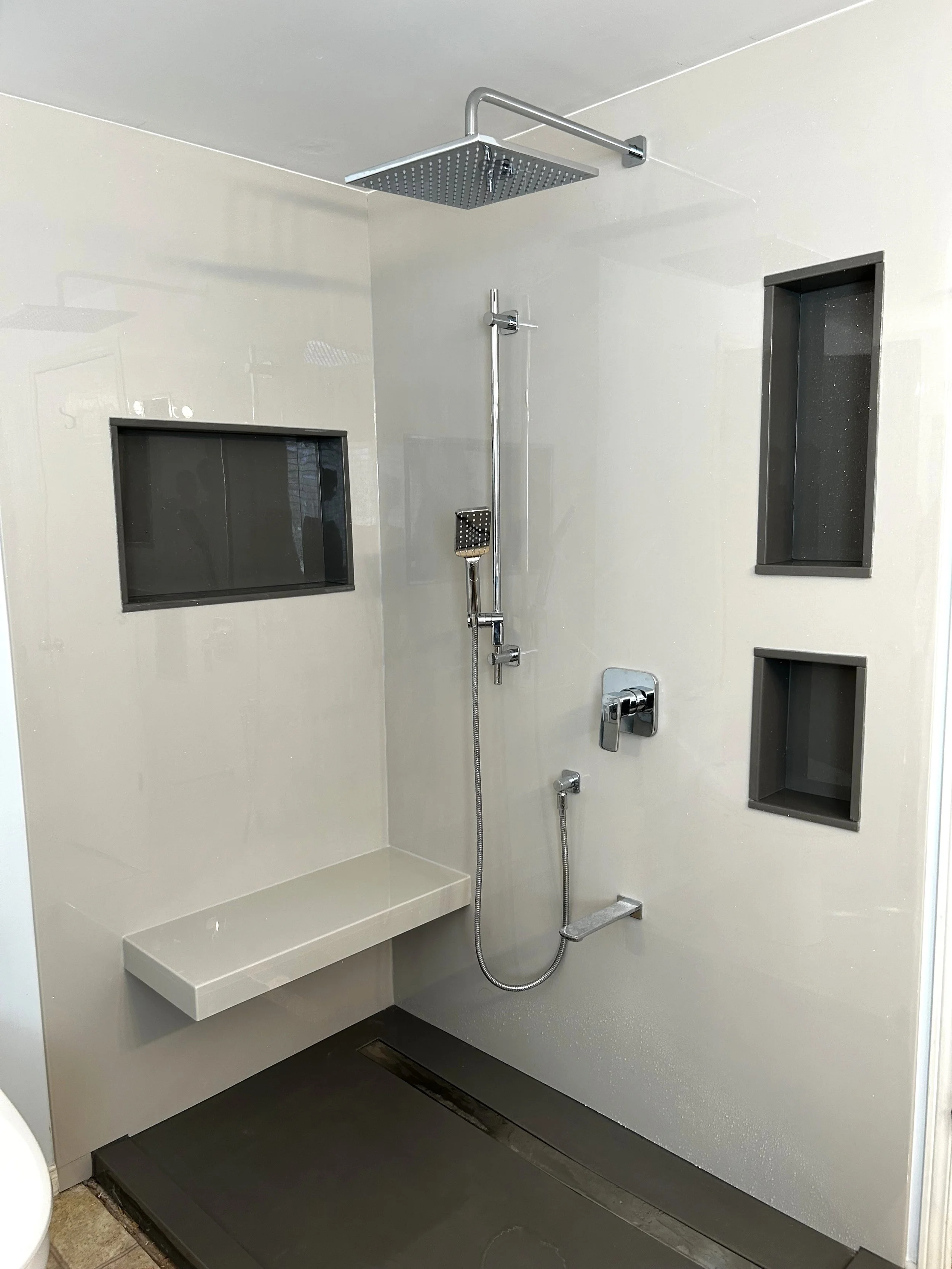 A modern shower with a rainfall showerhead, handheld shower, built-in wall niches, a bench, and a sleek design.