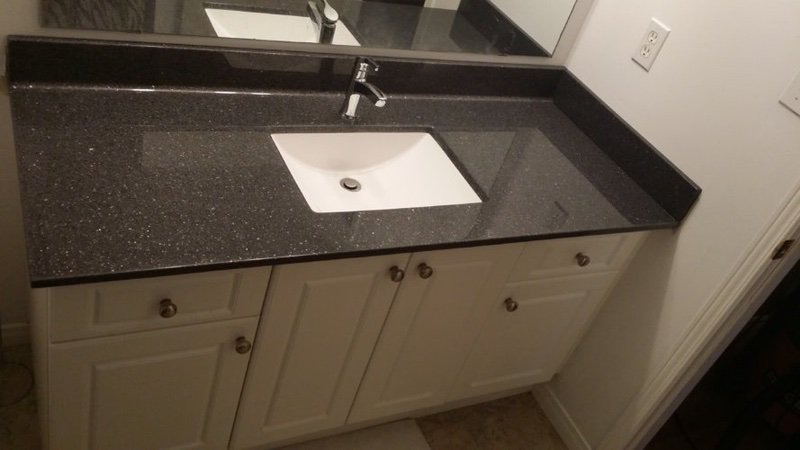 Bathroom vanity with a black granite countertop, a white rectangular sink, and a silver faucet. There are three white cabinet doors below the countertop, each with a round knob. A mirror is partially visible above the sink.